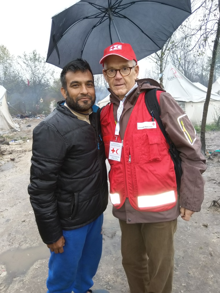Kaksi miestä  sateenvarjon alla pakolaisleirillä.
